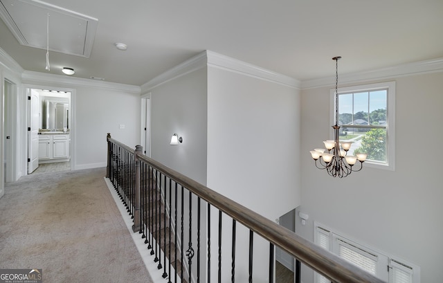 hall with attic access, an upstairs landing, crown molding, light colored carpet, and a chandelier
