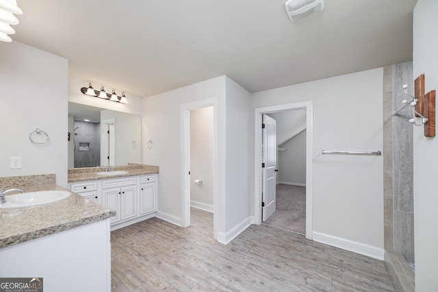 full bathroom featuring a tile shower, two vanities, wood finished floors, and baseboards