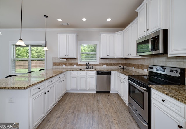 kitchen featuring appliances with stainless steel finishes, a peninsula, a sink, white cabinetry, and ornamental molding