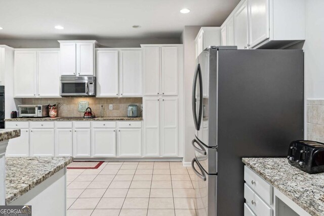 4960 Tadmore Ln, Lithonia, GA 30038 - kitchen with black appliances, white cabinets, decorative backsplash, light tile patterned floors, and light stone counters