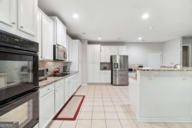 4960 Tadmore Ln, Lithonia, GA 30038 - kitchen featuring black appliances, a breakfast bar, decorative backsplash, light stone countertops, and white cabinets