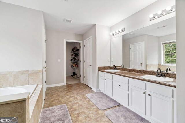 4960 Tadmore Ln, Lithonia, GA 30038 - full bathroom featuring double vanity, a walk in closet, a relaxing tiled tub, and baseboards