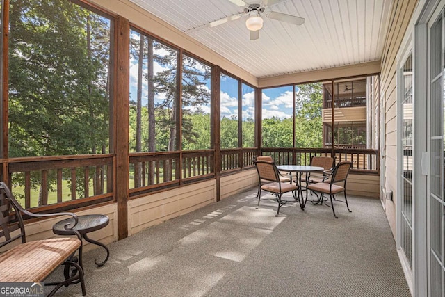 sunroom / solarium with ceiling fan, outdoor dining space, and view of wooded area