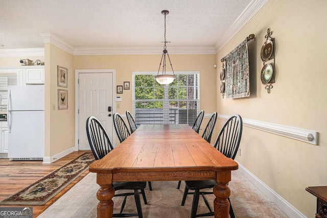 dining area with a textured ceiling, ornamental molding, light wood finished floors, and baseboards