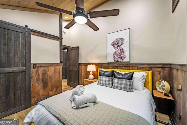 bedroom featuring a barn door, wood finished floors, a wainscoted wall, ceiling fan, and wood walls