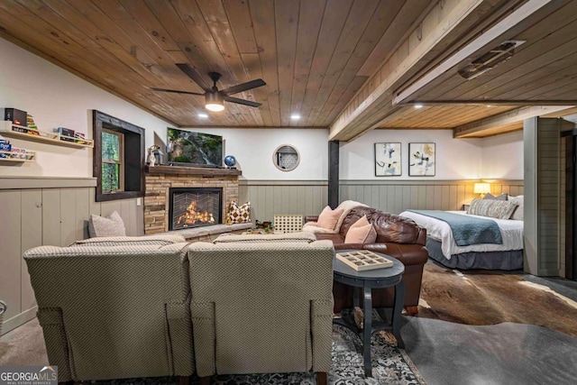 carpeted living room featuring a wainscoted wall, wood ceiling, a fireplace, and ceiling fan