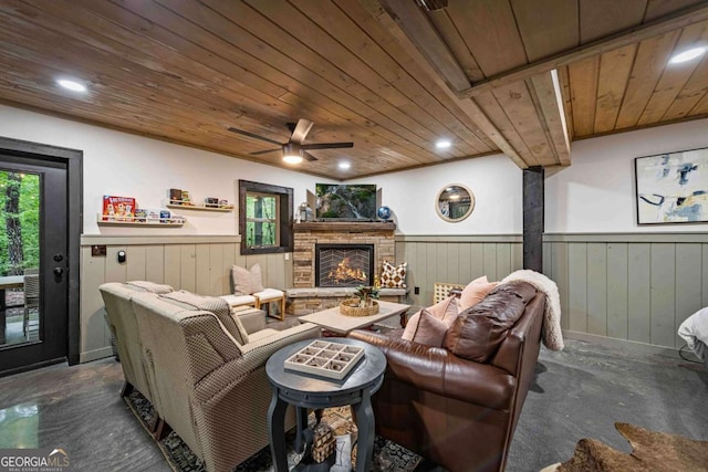 living area featuring wooden ceiling, a wainscoted wall, a ceiling fan, a stone fireplace, and wooden walls