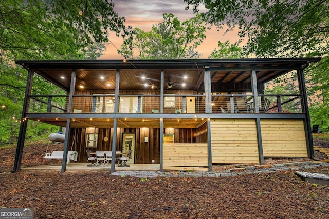back of house at dusk featuring a patio area and a wooden deck