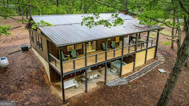 rear view of property with a patio area, metal roof, a deck, an attached garage, and central AC