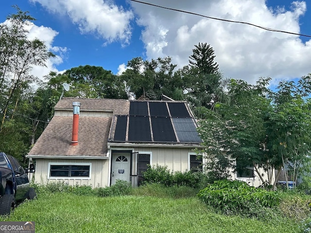 view of front of house with roof mounted solar panels, board and batten siding, a chimney, and roof with shingles
