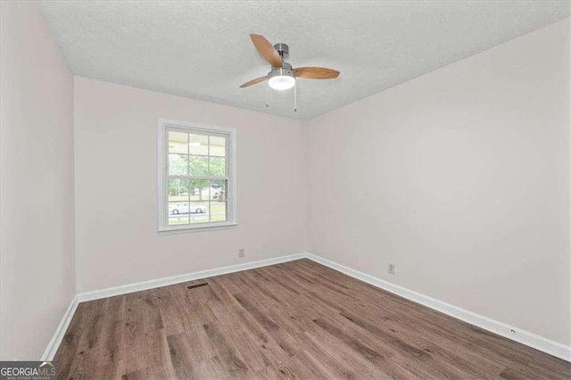 empty room featuring wood finished floors, baseboards, ceiling fan, and a textured ceiling