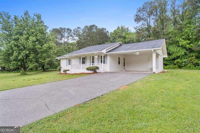 ranch-style house with driveway, a front lawn, an attached carport, a porch, and view of wooded area