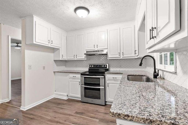 kitchen with double oven range, a sink, under cabinet range hood, white cabinetry, and light stone countertops