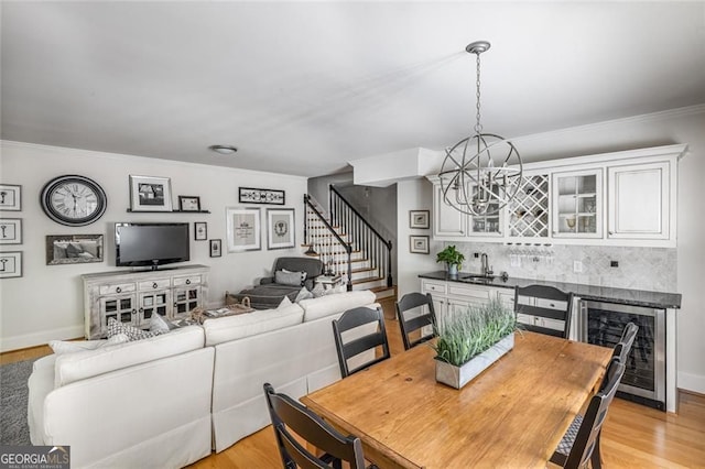 dining space with wine cooler, stairway, a chandelier, crown molding, and light wood finished floors