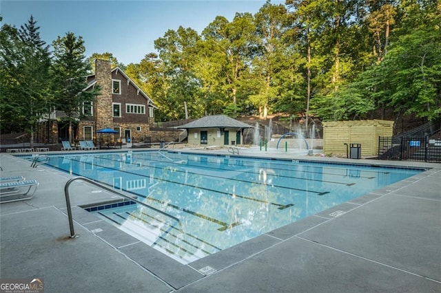 community pool with fence, a patio area, and view of scattered trees