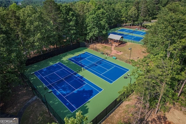 view of tennis court with fence and a forest view
