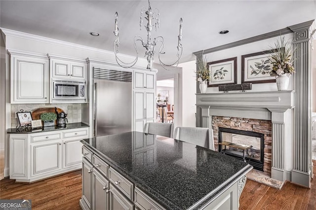 kitchen featuring built in appliances, dark wood-style floors, a fireplace, a chandelier, and tasteful backsplash