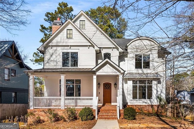 view of front of home with covered porch, a chimney, a standing seam roof, metal roof, and fence