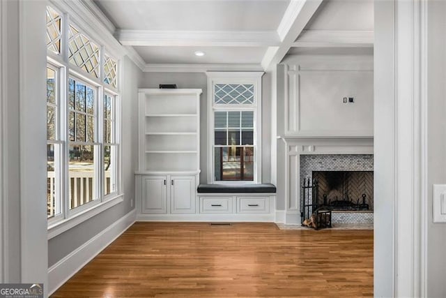 unfurnished living room featuring ornamental molding, wood finished floors, a tile fireplace, beamed ceiling, and baseboards