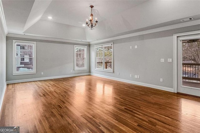 unfurnished living room with a raised ceiling, baseboards, a chandelier, crown molding, and wood finished floors