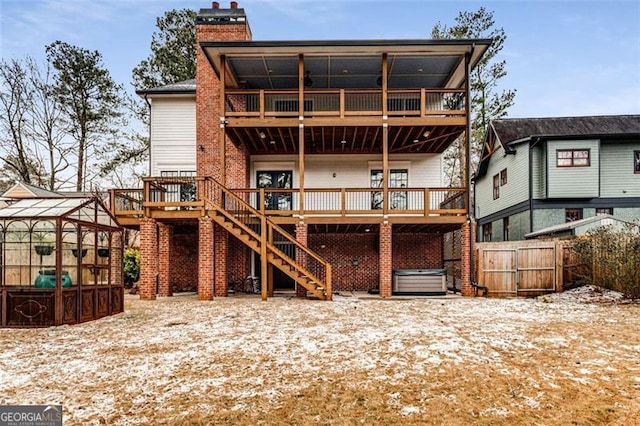 rear view of house featuring stairs, a chimney, a deck, fence, and a hot tub