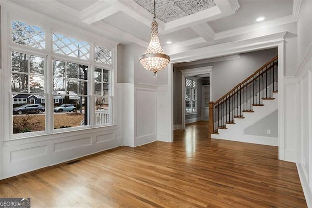unfurnished dining area with a decorative wall, a chandelier, stairway, wood finished floors, and coffered ceiling