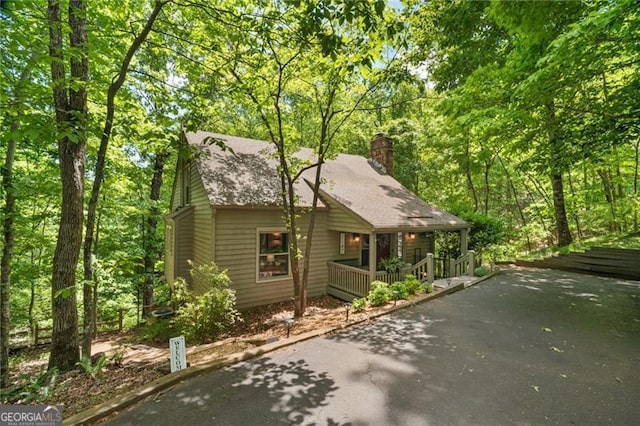 chalet / cabin with driveway, a chimney, covered porch, and roof with shingles