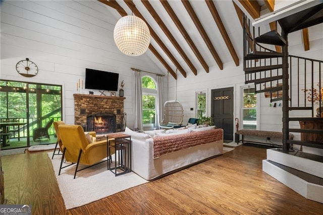 living room with wood finished floors, plenty of natural light, beam ceiling, a stone fireplace, and stairs