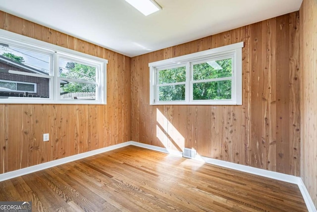 spare room featuring healthy amount of natural light, wood finished floors, baseboards, and wooden walls