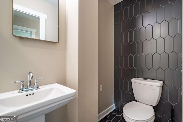 half bathroom with a sink, toilet, baseboards, and tile patterned floors