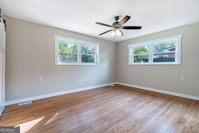 empty room with baseboards, wood finished floors, ceiling fan, and a barn door