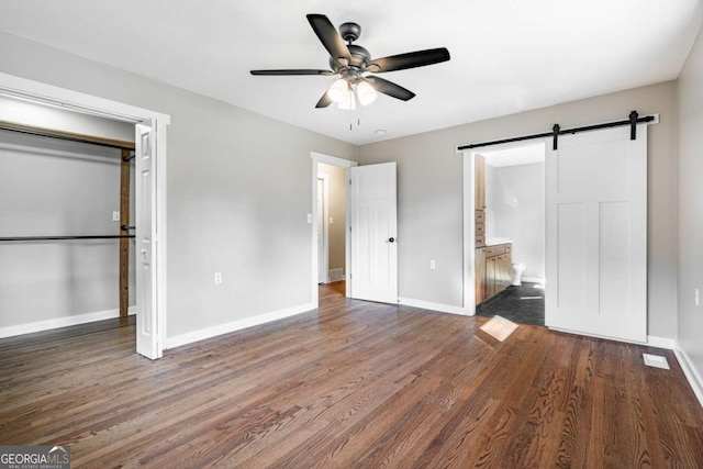 unfurnished bedroom with a barn door, baseboards, wood finished floors, and ensuite bathroom