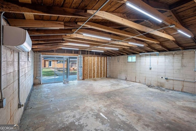 basement featuring a wall mounted air conditioner, concrete block wall, and a garage