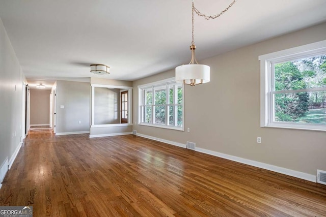 unfurnished dining area with healthy amount of natural light, wood finished floors, and baseboards