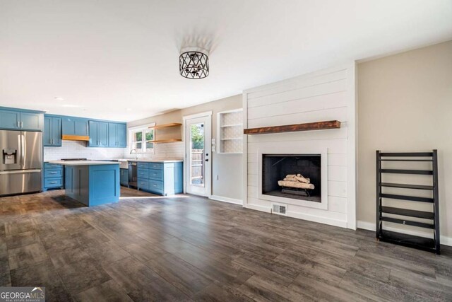 kitchen featuring appliances with stainless steel finishes, blue cabinetry, light countertops, dark wood-style flooring, and a kitchen island