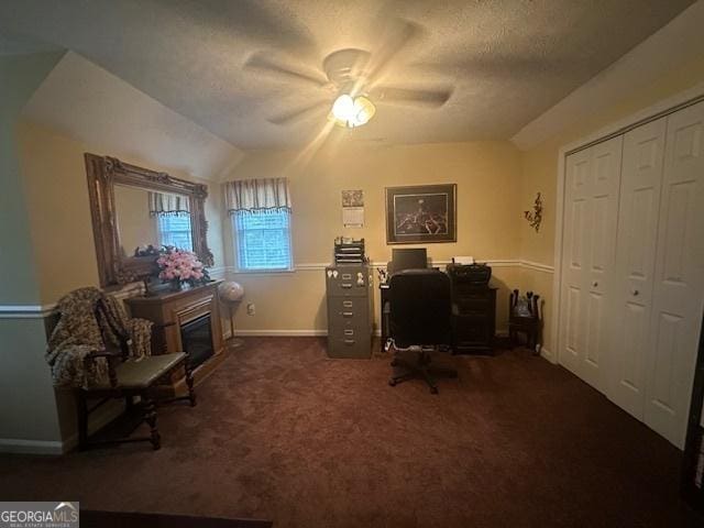 office featuring a ceiling fan, baseboards, a glass covered fireplace, carpet flooring, and lofted ceiling