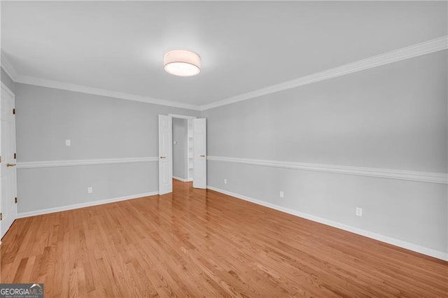 empty room with light wood-style floors, baseboards, and crown molding