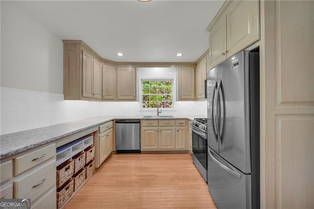 kitchen with appliances with stainless steel finishes, a sink, light wood-style floors, light stone countertops, and light brown cabinets
