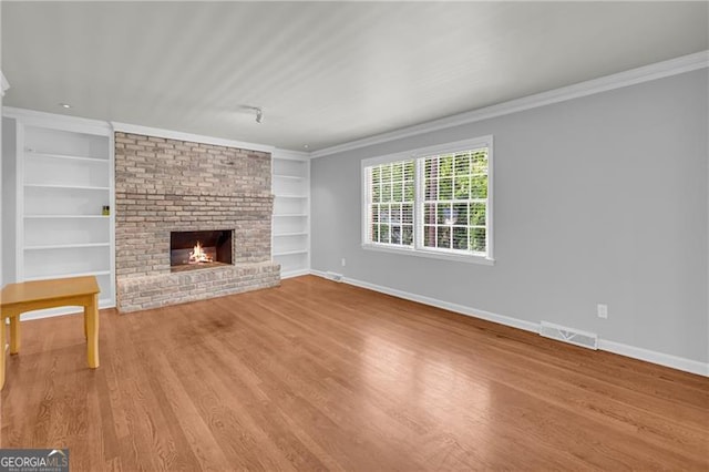 unfurnished living room with built in features, a fireplace, ornamental molding, baseboards, and wood finished floors