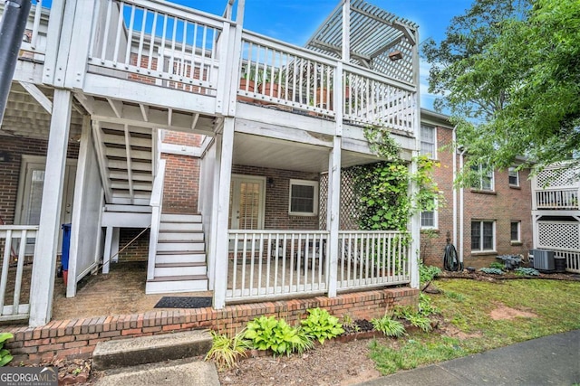 view of side of home featuring brick siding, central AC, stairs, and a balcony
