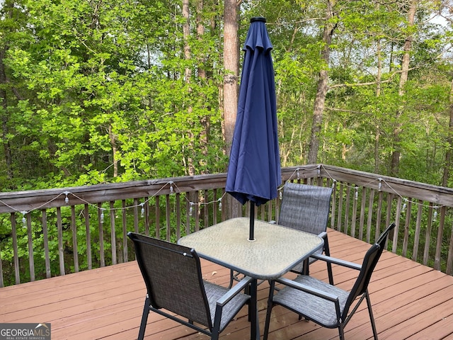 wooden terrace with outdoor dining area and a view of trees