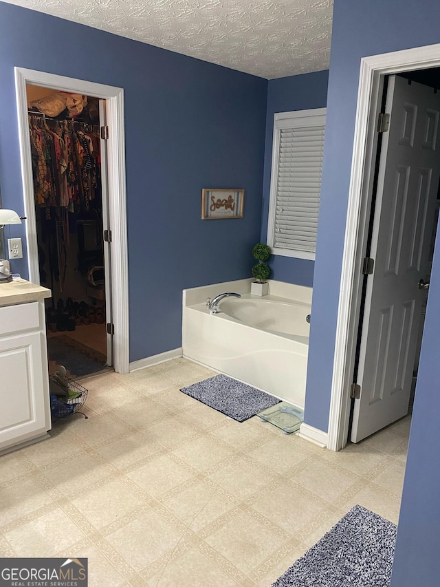 565 Miles Ct, Locust Grove, GA 30248 - bathroom with a bath, a textured ceiling, baseboards, a walk in closet, and vanity