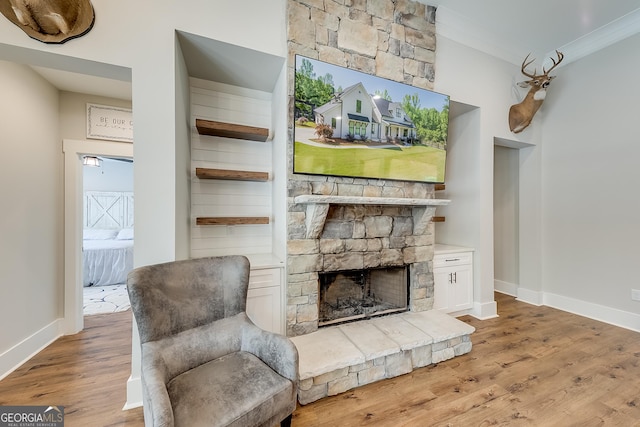 sitting room featuring wood finished floors, baseboards, ornamental molding, and a stone fireplace
