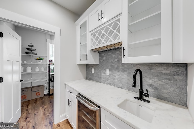 kitchen featuring beverage cooler, a sink, decorative backsplash, glass insert cabinets, and light wood-style flooring