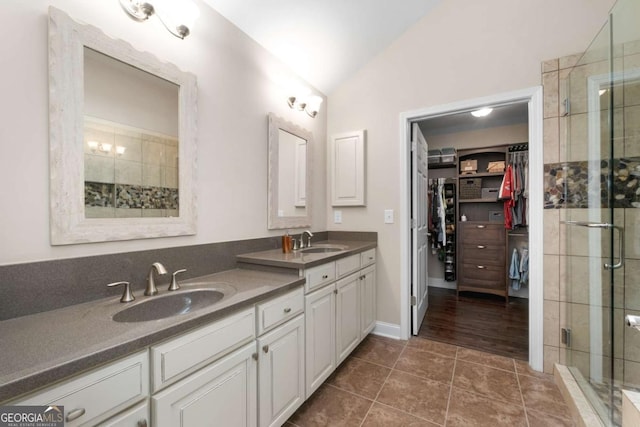 bathroom featuring vaulted ceiling, a shower stall, double vanity, a spacious closet, and tile patterned flooring