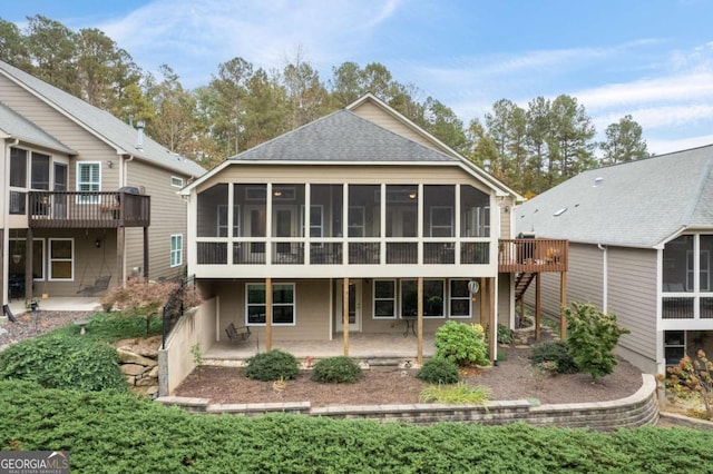 rear view of house with a sunroom, a patio area, roof with shingles, and a wooden deck