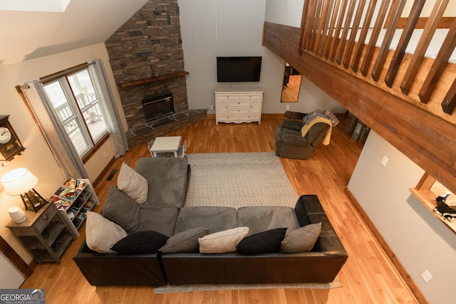 living area featuring wood finished floors, a stone fireplace, lofted ceiling, and baseboards