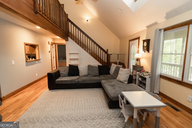 living area featuring light wood-style floors, stairs, baseboards, a towering ceiling, and a skylight