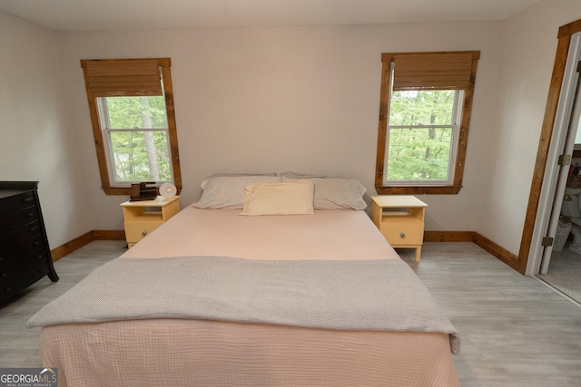 bedroom featuring multiple windows, baseboards, and light wood-style floors