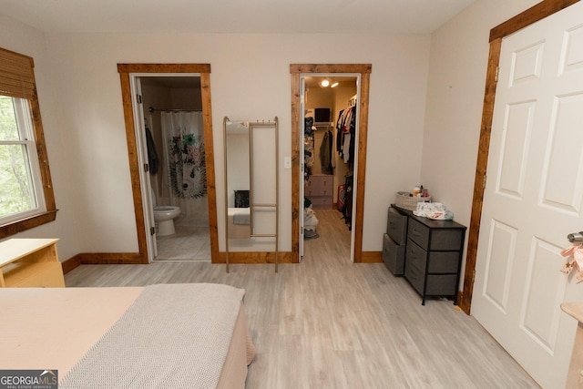 bedroom with a spacious closet, baseboards, light wood-style floors, a closet, and ensuite bath